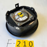 A used black circular automotive or machinery component with a visible metal motor assembly and yellow wire connector, resting on a white table with yellow inventory tags and handwritten 'F-210' notation.